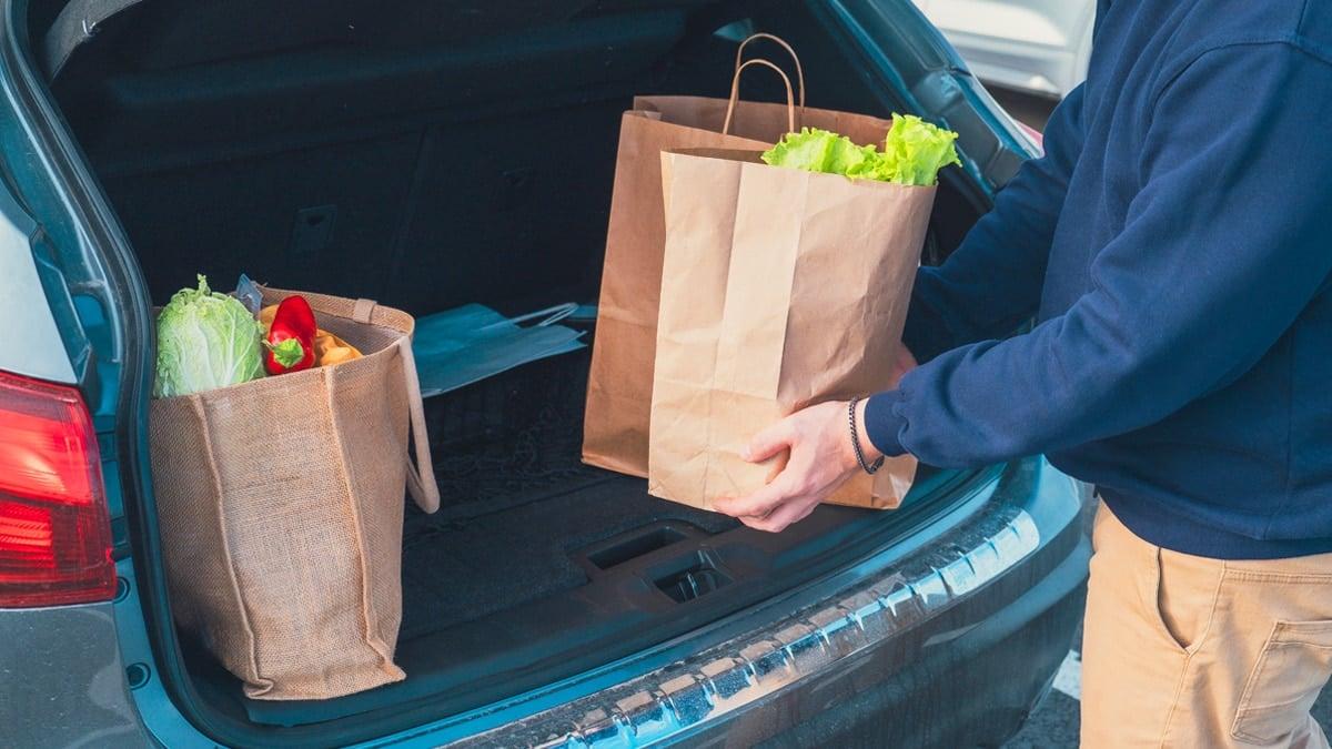 Volle Einkaufstaschen werden in einen offenen Kofferraum geladen